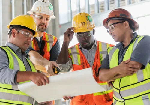 Construction workers review blueprints on site.