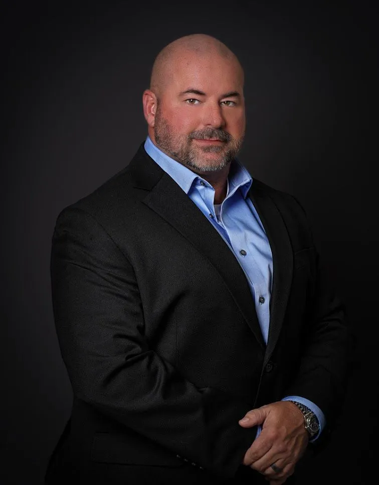 Man in suit with beard and blue shirt.