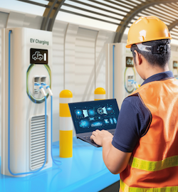 Worker inspecting EV charging station with laptop.