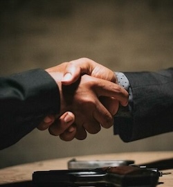 Two men shaking hands over a gun.